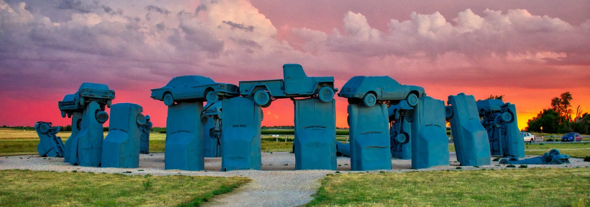Carhenge with a beautiful sunset with orange, pink and purple sky.
